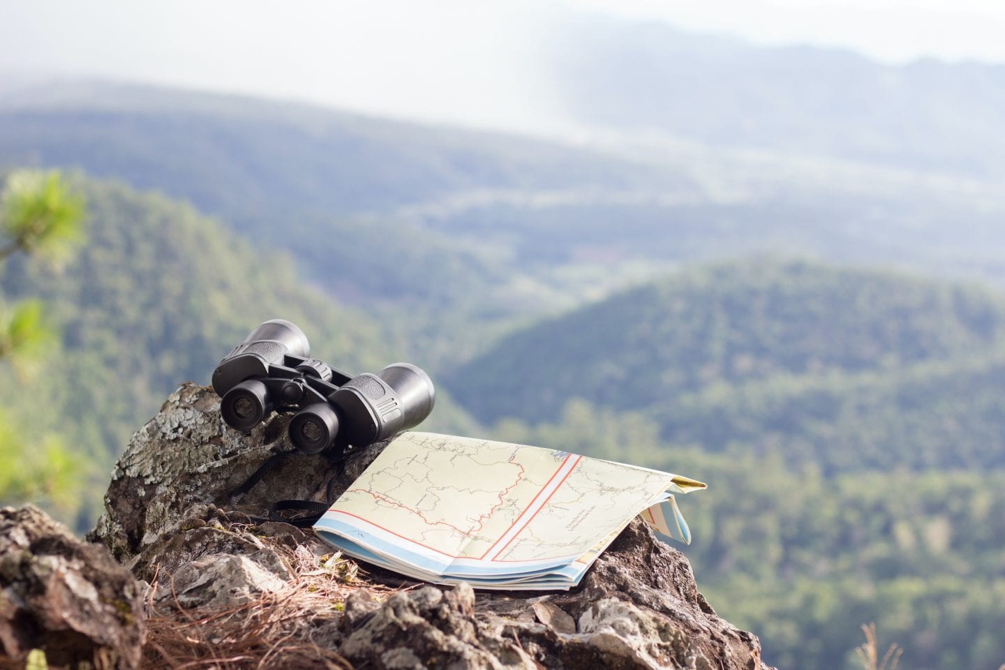 Binoculars and hiking maps on rocky cliffs with landscape