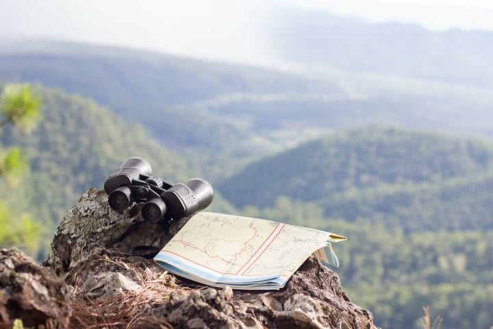 Binoculars and hiking maps on rocky cliffs with landscape