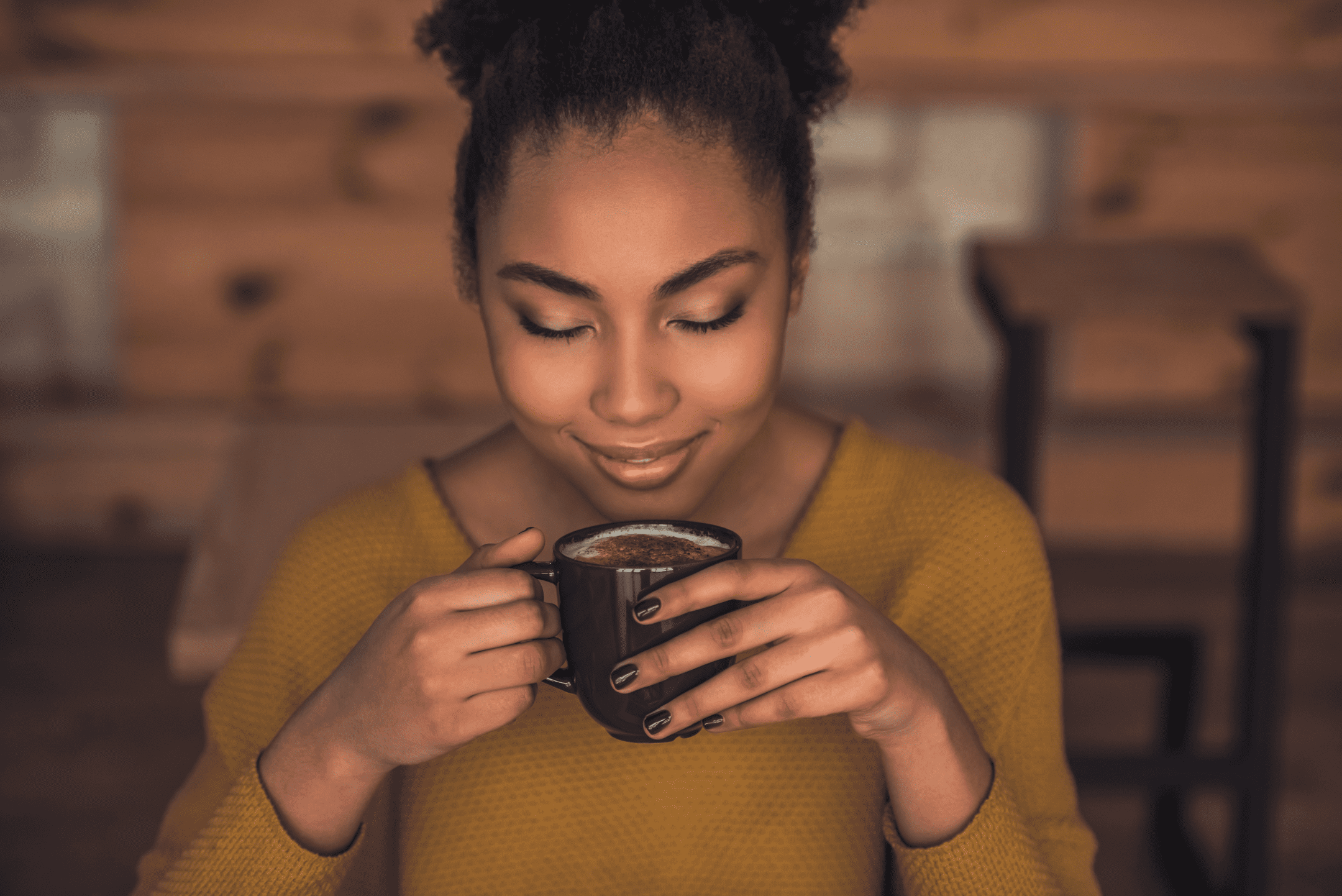woman wearing yellow shirt smiles while inhaling cup of coffee